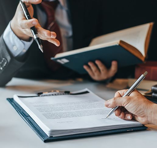person holding out a book while another person signs paperwork